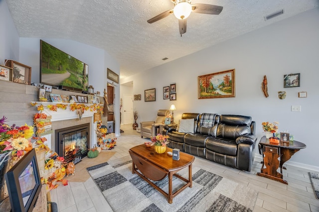 living room with a tiled fireplace, ceiling fan, and a textured ceiling