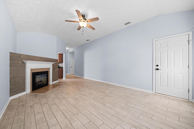 unfurnished living room with a textured ceiling, ceiling fan, light wood-type flooring, a glass covered fireplace, and vaulted ceiling