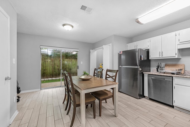 kitchen with light hardwood / wood-style floors, white cabinetry, appliances with stainless steel finishes, and a textured ceiling