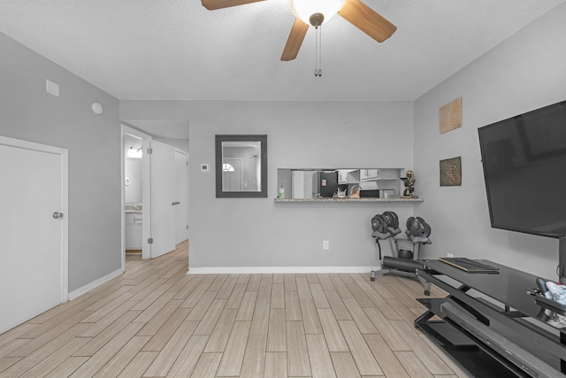 workout room featuring ceiling fan, light hardwood / wood-style flooring, and a textured ceiling