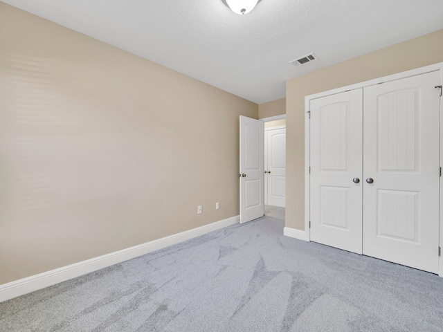 unfurnished bedroom featuring a closet, light carpet, and a textured ceiling