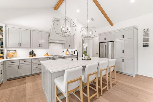 kitchen featuring custom exhaust hood, beam ceiling, stainless steel appliances, and a center island with sink