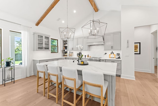 kitchen with light stone counters, a kitchen breakfast bar, light hardwood / wood-style floors, beam ceiling, and a center island with sink