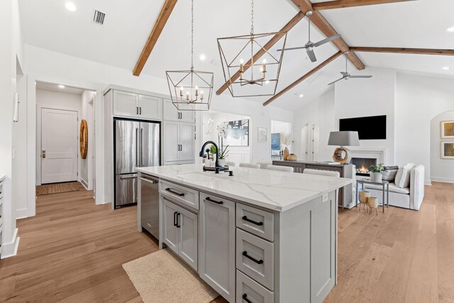 kitchen with gray cabinetry, stainless steel appliances, light hardwood / wood-style flooring, and an island with sink