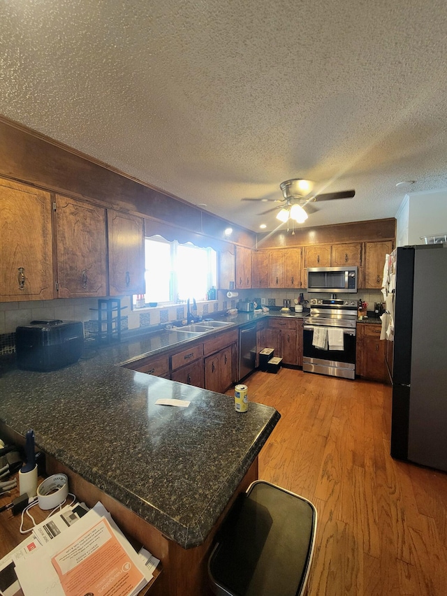 kitchen featuring stainless steel appliances, light wood-type flooring, a textured ceiling, kitchen peninsula, and ceiling fan