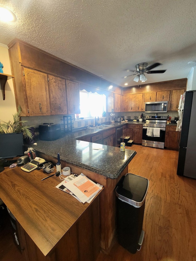 kitchen with stainless steel appliances, a textured ceiling, sink, kitchen peninsula, and light hardwood / wood-style flooring