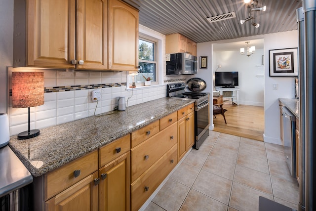 kitchen with dark stone counters, light tile patterned floors, backsplash, pendant lighting, and appliances with stainless steel finishes