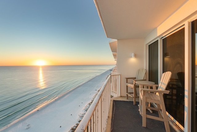 balcony at dusk featuring a water view and a beach view