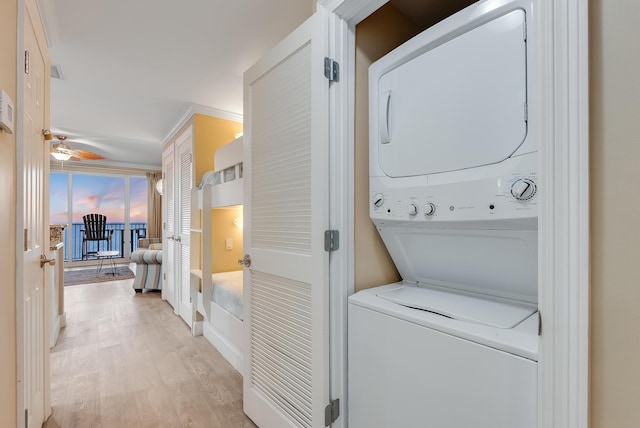 clothes washing area with laundry area, ceiling fan, stacked washer / dryer, and light wood-style floors