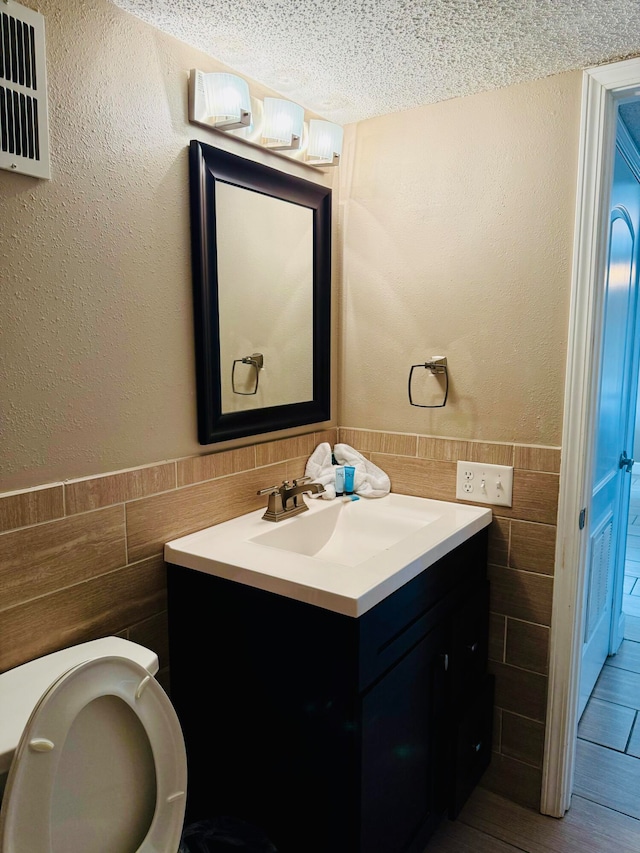 bathroom with vanity, a textured ceiling, toilet, and tile walls