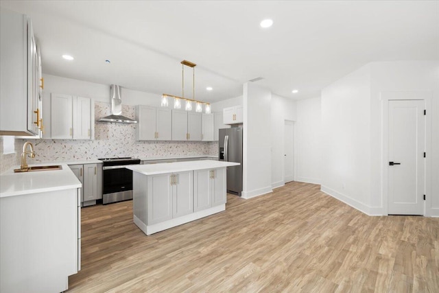 kitchen featuring wall chimney range hood, hanging light fixtures, a kitchen island, sink, and stainless steel appliances