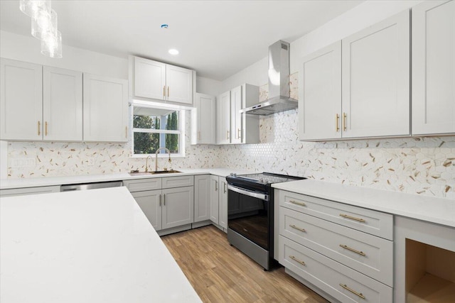 kitchen featuring wall chimney range hood, sink, light wood-type flooring, stainless steel appliances, and decorative light fixtures