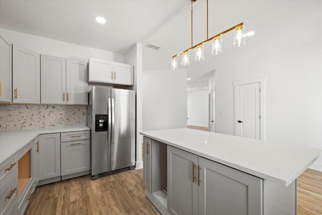 kitchen featuring gray cabinetry, wood-type flooring, stainless steel fridge, pendant lighting, and tasteful backsplash