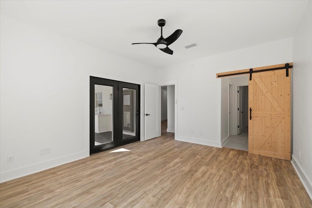 unfurnished room with ceiling fan, light wood-type flooring, and a barn door