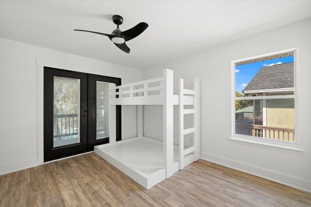 unfurnished bedroom with multiple windows, french doors, access to exterior, and wood-type flooring