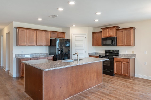 kitchen with black appliances, sink, light wood-type flooring, and a kitchen island with sink