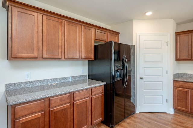 kitchen featuring light hardwood / wood-style floors, light stone counters, and black fridge