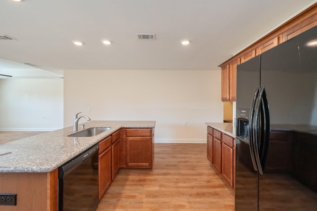 kitchen featuring an island with sink, light stone countertops, black appliances, light hardwood / wood-style floors, and sink