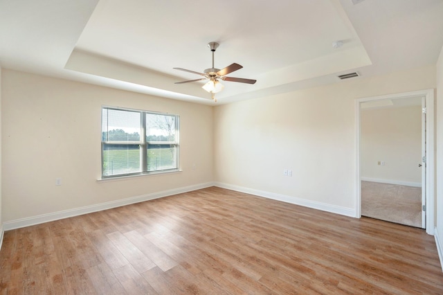 empty room with light hardwood / wood-style flooring, a tray ceiling, and ceiling fan