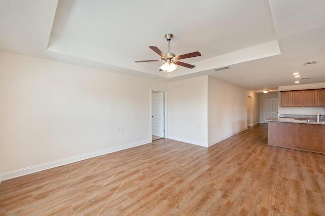 unfurnished living room featuring sink, a raised ceiling, light wood-type flooring, and ceiling fan