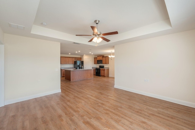 unfurnished living room with light hardwood / wood-style flooring, a tray ceiling, and ceiling fan with notable chandelier