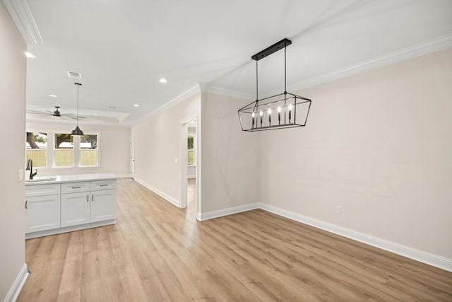 unfurnished dining area featuring ceiling fan with notable chandelier, sink, crown molding, and light hardwood / wood-style floors