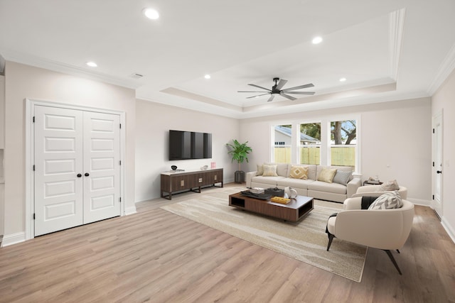 living room featuring a raised ceiling, ceiling fan, crown molding, and light hardwood / wood-style floors