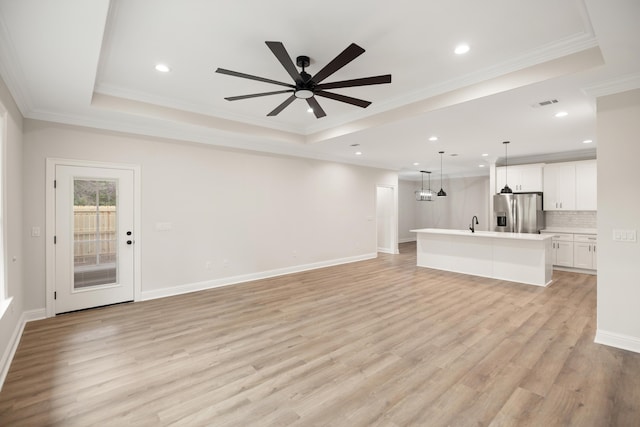 unfurnished living room featuring a raised ceiling, ceiling fan, ornamental molding, and light hardwood / wood-style floors