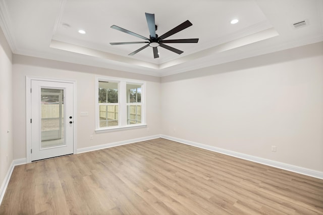 empty room with ceiling fan, a tray ceiling, light hardwood / wood-style flooring, and crown molding