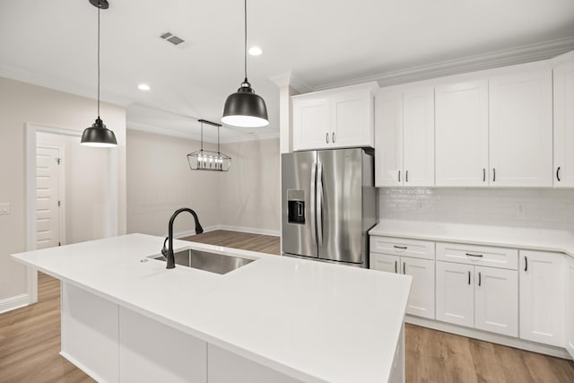 kitchen with white cabinetry, stainless steel fridge, an island with sink, decorative light fixtures, and sink