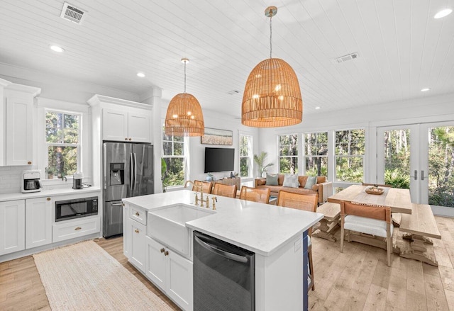 kitchen with white cabinets, an island with sink, appliances with stainless steel finishes, light hardwood / wood-style flooring, and pendant lighting