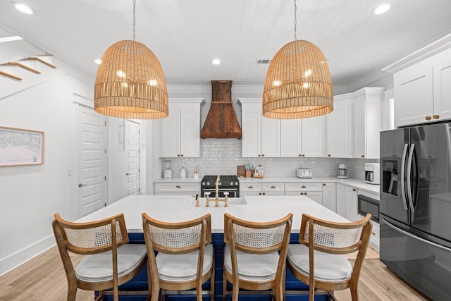 kitchen featuring custom range hood, decorative light fixtures, white cabinetry, appliances with stainless steel finishes, and light hardwood / wood-style floors