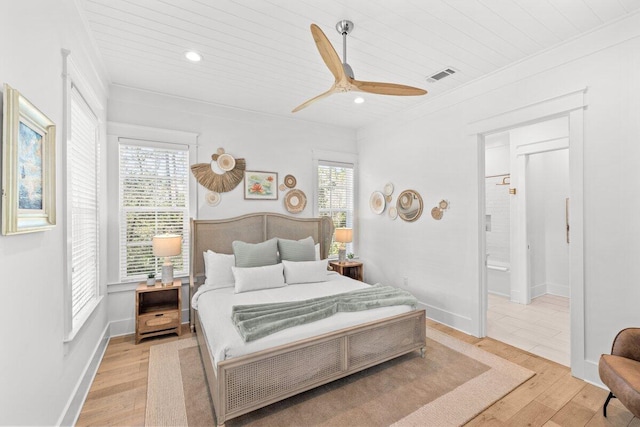 bedroom featuring light hardwood / wood-style floors, multiple windows, ensuite bathroom, and ceiling fan