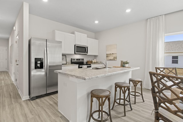 kitchen with light wood-type flooring, appliances with stainless steel finishes, white cabinetry, and a center island with sink