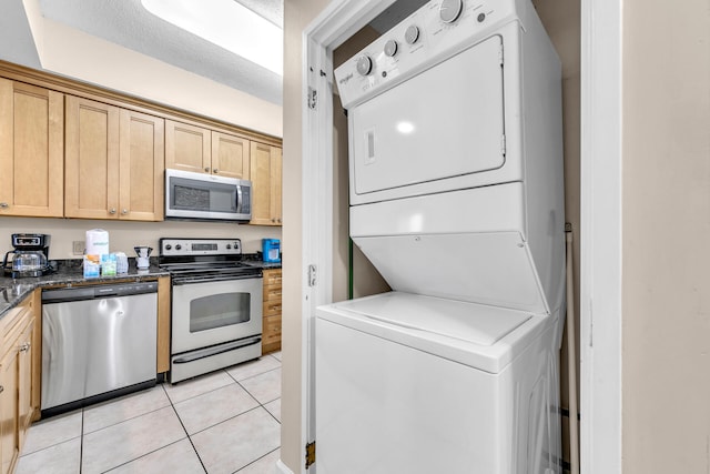 kitchen featuring light brown cabinetry, a textured ceiling, stainless steel appliances, stacked washer / drying machine, and light tile patterned floors