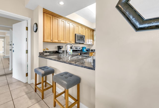 kitchen with a kitchen breakfast bar, stainless steel appliances, light tile patterned floors, and dark stone counters