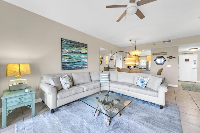 tiled living room with ceiling fan with notable chandelier