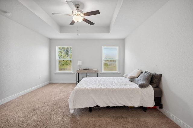 bedroom with light carpet, a tray ceiling, and ceiling fan