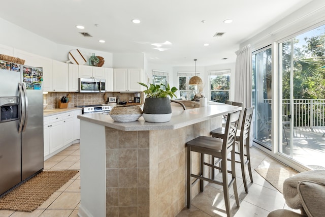 kitchen with white cabinets, stainless steel appliances, an island with sink, and hanging light fixtures