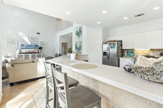 kitchen featuring stainless steel fridge, recessed lighting, white cabinetry, backsplash, and visible vents
