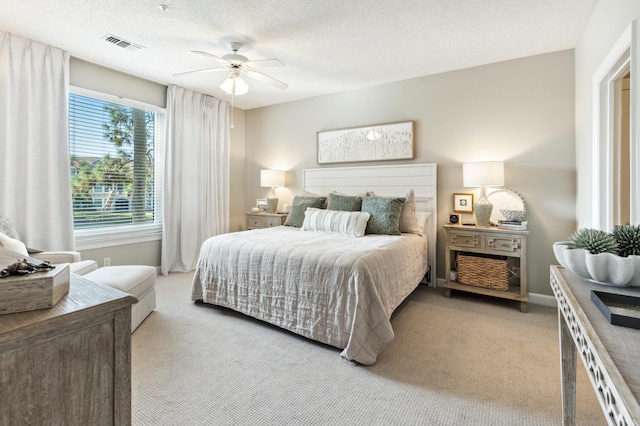 bedroom with ceiling fan, a textured ceiling, visible vents, baseboards, and light carpet