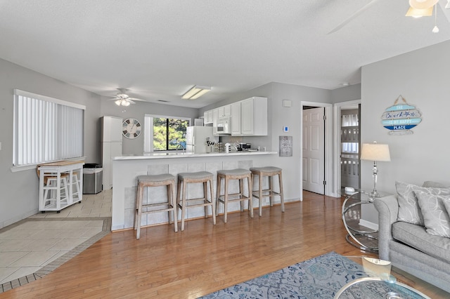 285 Payne St Unit 20B, Miramar Beach, FL 32550 - kitchen featuring white appliances, ceiling fan, a breakfast bar, light wood-style floors, and white cabinets