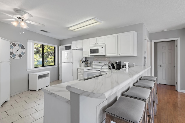 kitchen featuring white appliances, light wood-type flooring, a breakfast bar area, and kitchen peninsula