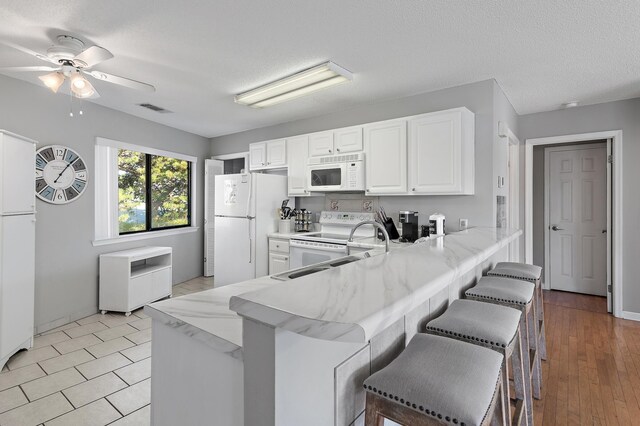 285 Payne St Unit 20B, Miramar Beach, FL 32550 - kitchen with white appliances, ceiling fan, a peninsula, a kitchen bar, and white cabinetry