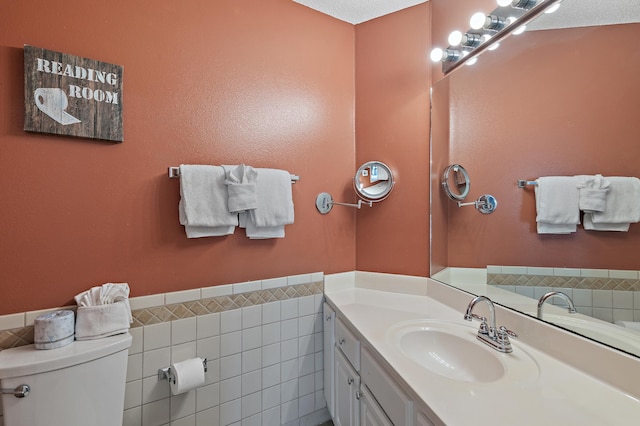 bathroom featuring toilet, a textured ceiling, vanity, and tile walls