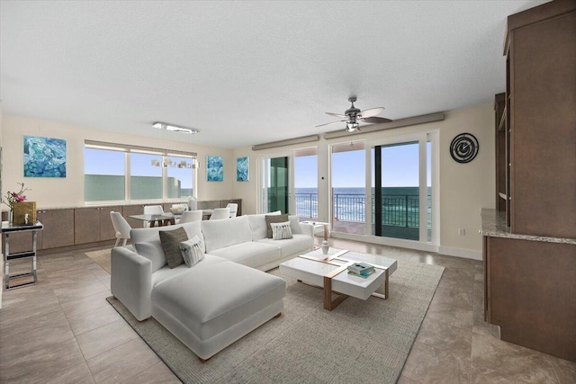 living area featuring a textured ceiling, ceiling fan, a water view, and baseboards