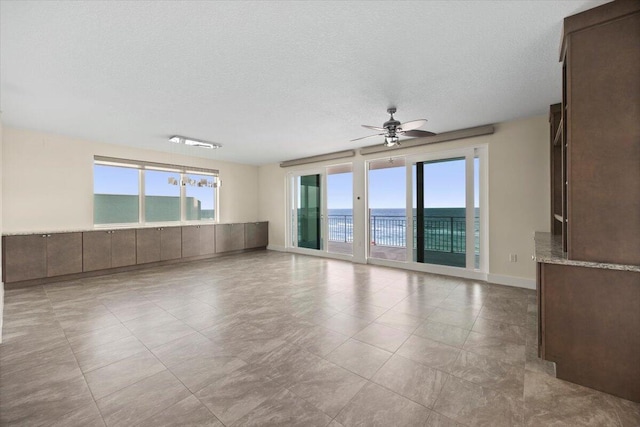 spare room featuring ceiling fan, a textured ceiling, a water view, and baseboards