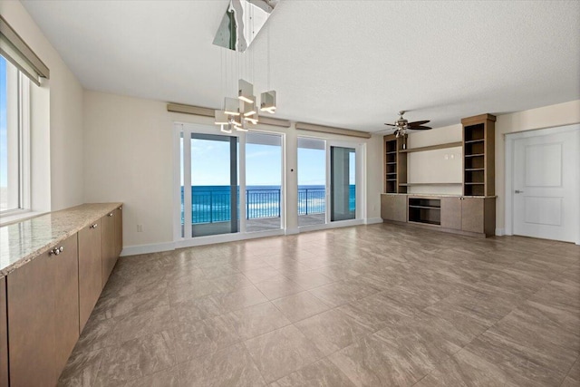 unfurnished living room with a water view, a textured ceiling, baseboards, and ceiling fan with notable chandelier