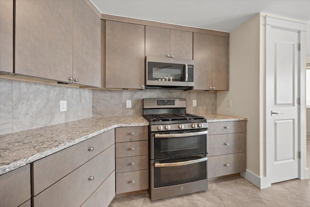 kitchen with light tile patterned floors, light stone counters, stainless steel appliances, baseboards, and backsplash