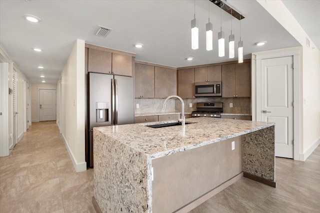 kitchen with visible vents, hanging light fixtures, appliances with stainless steel finishes, an island with sink, and light stone countertops